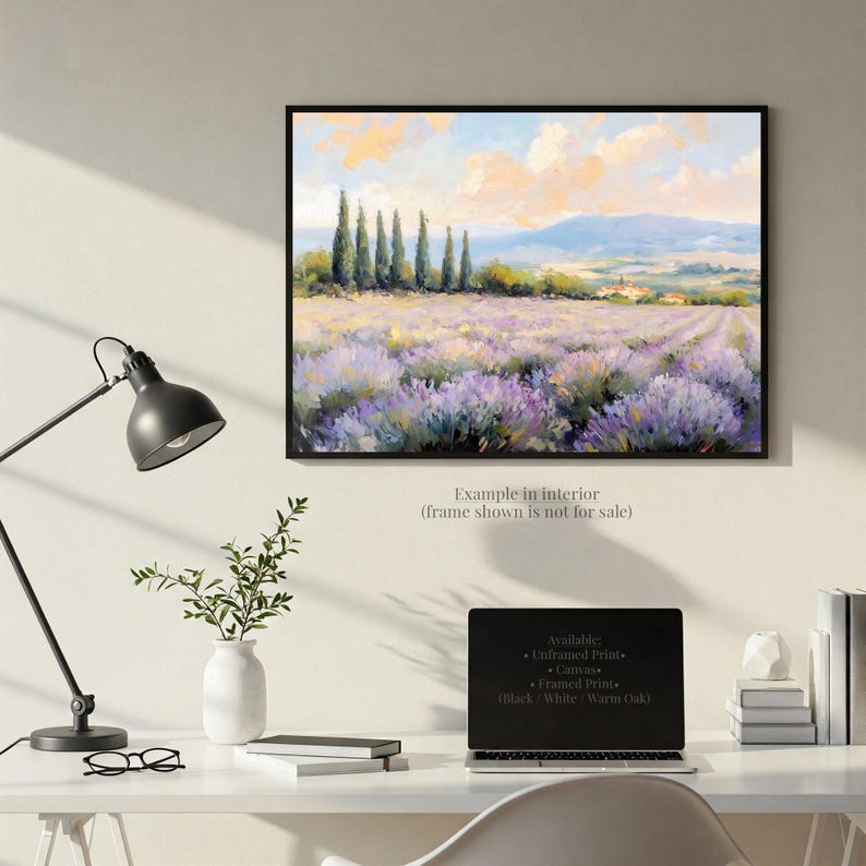a painting of a field of lavender flowers hanging on a wall above a desk with a laptop, books, and a plant.