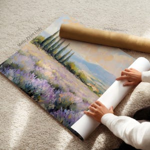 A person is holding a roll of paper and a painting of a field of purple flowers, with the person's hands visible as they roll up the paper.