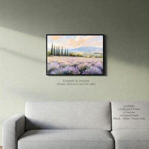 a painting of a field of lavender flowers hanging on a wall above a gray couch.