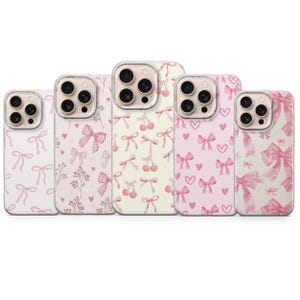 May include: A collection of five phone cases with various patterns. The cases feature designs of pink bows, cherries, and hearts on a white or light pink background. The cases have a clear border around the camera.