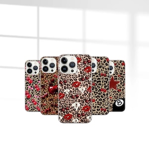 May include: A collection of phone cases with various designs. The cases feature a leopard print background with red cherries, red lips, and a red star. One case has an eight ball graphic. The cases are designed for a smartphone.