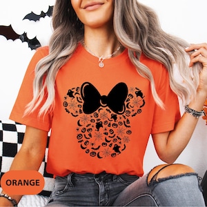 May include: Orange t-shirt featuring a black bow and a Halloween-themed design in the shape of a mouse head. The design includes bats, spiderwebs, ghosts, and pumpkins. The word "ORANGE" is printed at the bottom.