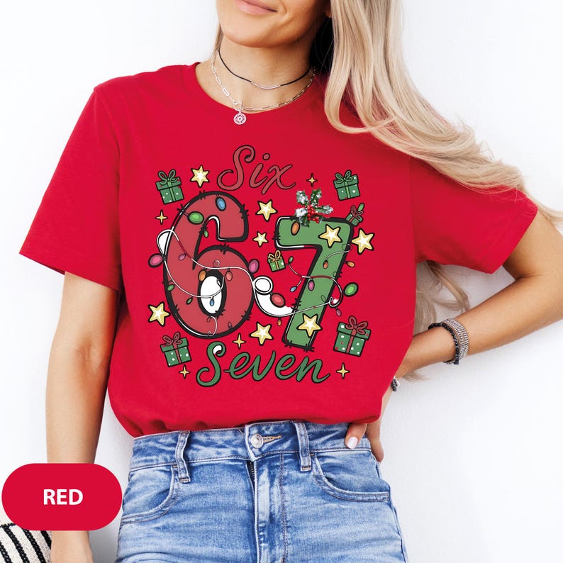 May include: A red t-shirt with the words "Six Seven" in a festive design. The numbers are decorated with Christmas lights and surrounded by stars and gift boxes. The shirt is a solid red color.