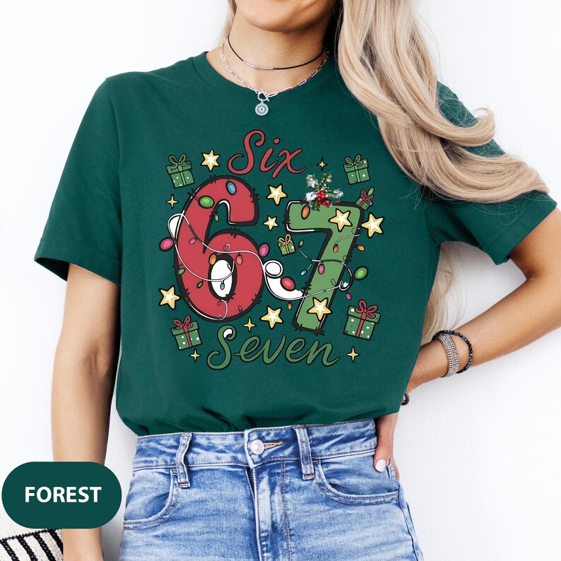 May include: Forest green t-shirt with a festive design. The graphic features the numbers "6" and "7" decorated with Christmas lights, stars, and gift boxes. The word "Six" and "Seven" are also included in the design.