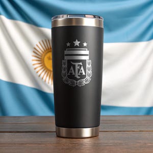 May include: A black insulated tumbler with a silver rim and base. The tumbler features a silver emblem with the letters "AFA" and three stars, set against the backdrop of the Argentinian flag.