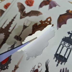 May include: A sheet of vampire-themed stickers featuring bats, roses, and gothic elements. The stickers are being peeled with tweezers. The text "vampire sticker sheet" is visible at the top.