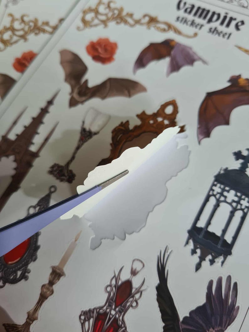 May include: A sheet of vampire-themed stickers featuring bats, roses, and gothic elements. The stickers are being peeled with tweezers. The text "vampire sticker sheet" is visible at the top.