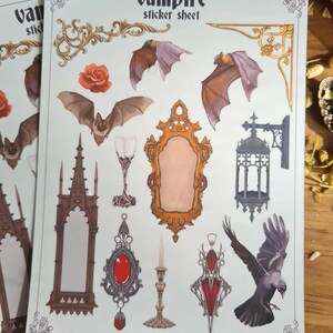 May include: A sticker sheet with a vampire theme. The sheet features illustrations of bats, a mirror, a raven, a rose, a goblet, and other gothic-style elements. The text "Vampire sticker sheet" is at the top. The website "ravenwood.store" is at the bottom.