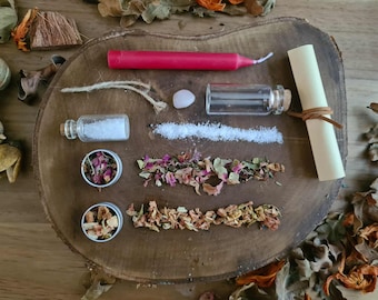 May include: A collection of ritual items arranged on a wooden surface. Includes a red candle, small glass bottles, a scroll, a small stone, and dried herbs and flowers. The items are arranged in a visually appealing manner, suggesting a spiritual or crafting theme.