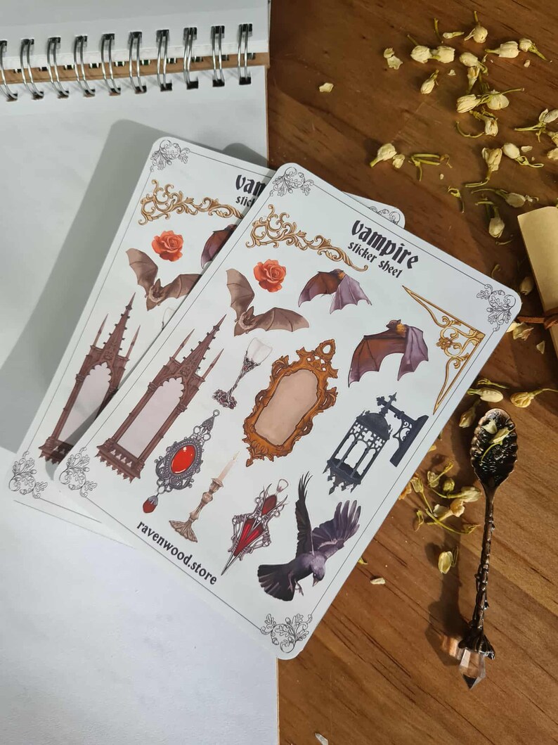 May include: Two sticker sheets with a vampire theme. The sheets feature bats, roses, gothic architecture, mirrors, and a raven. The text "vampire sticker sheet" and "ravenwood.store" are visible on the sheets. The stickers are on a wooden surface.