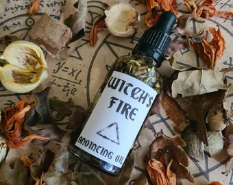 Pode incluir: Uma garrafa de vidro com conta-gotas preto, rotulada "Witch's Fire Anointing Oil", rodeada por folhas e flores secas. O rótulo apresenta um triângulo e texto preto. O fundo é uma superfície semelhante a pergaminho com escrita manuscrita.