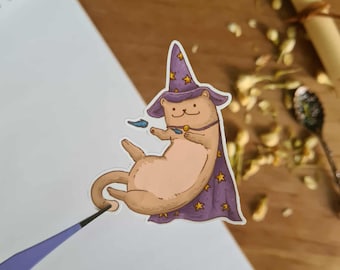 Könnte beinhalten: Ein skurriler Aufkleber mit einem Cartoon-Otter, der als Zauberer verkleidet ist und einen lila Hut und Umhang mit goldenen Sternen trägt. Der Otter ist hellbraun mit einem cremefarbenen Bauch und hält ein kleines blaues Objekt. Der Aufkleber befindet sich auf einer weißen Oberfläche.