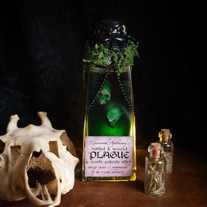 May include: A glass bottle with green liquid and a skull design, labelled "PLAGUE." The bottle has a black cap, moss, and a chain. Two small bottles with corks and a skull are also visible. The text reads "Ravenwood Apothecary's bottled & secured."