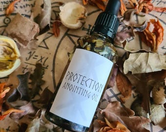 Könnte beinhalten: Eine Glasflasche mit Salböl und schwarzer Pipette, beschriftet mit "PROTECTION ANOINTING OIL". Die Flasche ist von getrockneten Blättern und Pflanzen in Braun-, Orange- und Beigetönen umgeben. Der Hintergrund zeigt handschriftliche Schrift.