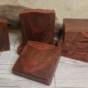 May include: A stack of six brown and red handmade soap bars with a marbled swirl pattern.