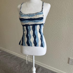 Könnte beinhalten: Ein gehäkeltes Oberteil mit einem weißen, blauen und marineblauen Streifenmuster. Das Oberteil hat eine lockere Passform und einen runden Ausschnitt.