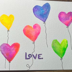 May include: A watercolor painting of six heart-shaped balloons in different colors, including yellow, pink, purple, blue, and green. The balloons are tied together with strings and the word "LOVE" is written in purple below them.