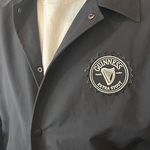 May include: A black jacket with a white Guinness logo featuring a harp and the text "TRADE MARK EXTRA STOUT" on the right side of the chest.