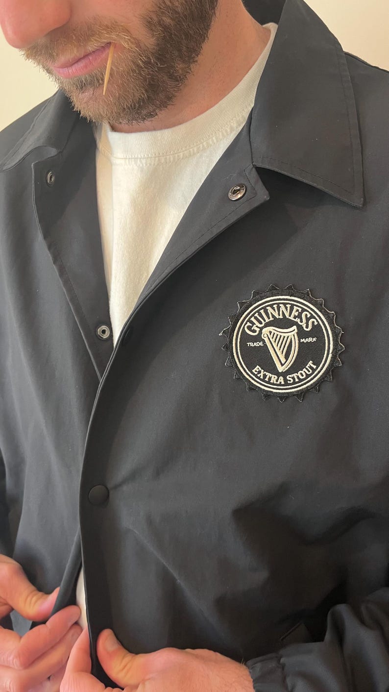 May include: A black jacket with a white Guinness logo featuring a harp and the text "TRADE MARK EXTRA STOUT" on the right side of the chest.