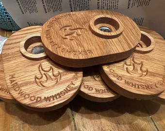 May include: A stack of wooden whiskey smokers with a natural wood grain finish. Each smoker has a circular opening and engraved text that reads "Hardwood Whiskey Smoker". The design includes a flame graphic.
