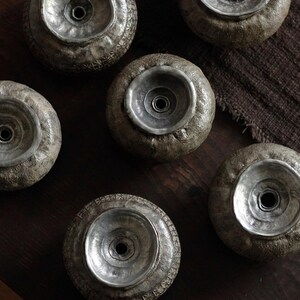 May include: A collection of six decorative, wheel-shaped objects with a textured, gray exterior and a silver-colored, bowl-like center. The objects are arranged on a dark wooden surface, creating a rustic aesthetic. The silver centers have a central hole.