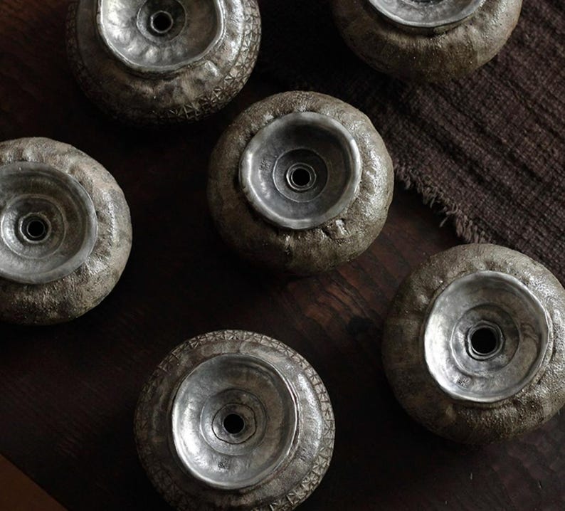 May include: A collection of six decorative, wheel-shaped objects with a textured, gray exterior and a silver-colored, bowl-like center. The objects are arranged on a dark wooden surface, creating a rustic aesthetic. The silver centers have a central hole.