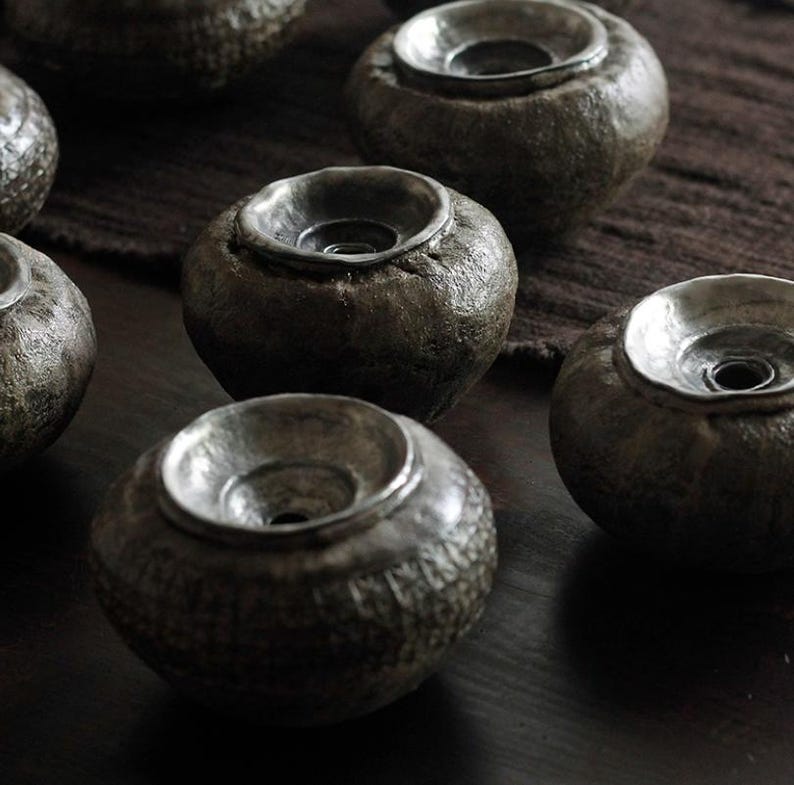 May include: A collection of small, dark gray ceramic bowls with a textured exterior and a smooth, silver-colored interior. The bowls have a rounded shape with a wide, shallow opening. The bowls are arranged on a dark brown surface.