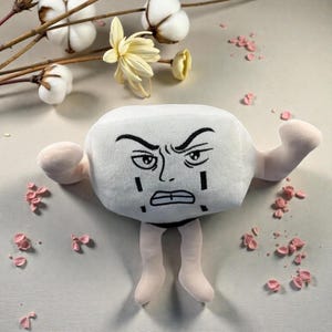 May include: A white plush toy with a stern, cartoon face, black eyebrows, and black markings. The toy has light pink arms and legs, and is set against a neutral background with floral accents. A unique and expressive plushie.