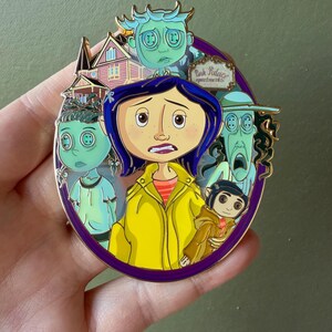 May include: A round enamel pin featuring characters from the animated film, "Coraline." The pin has a purple border and depicts the main character in a yellow raincoat, surrounded by other characters and the Pink Palace Apartments.