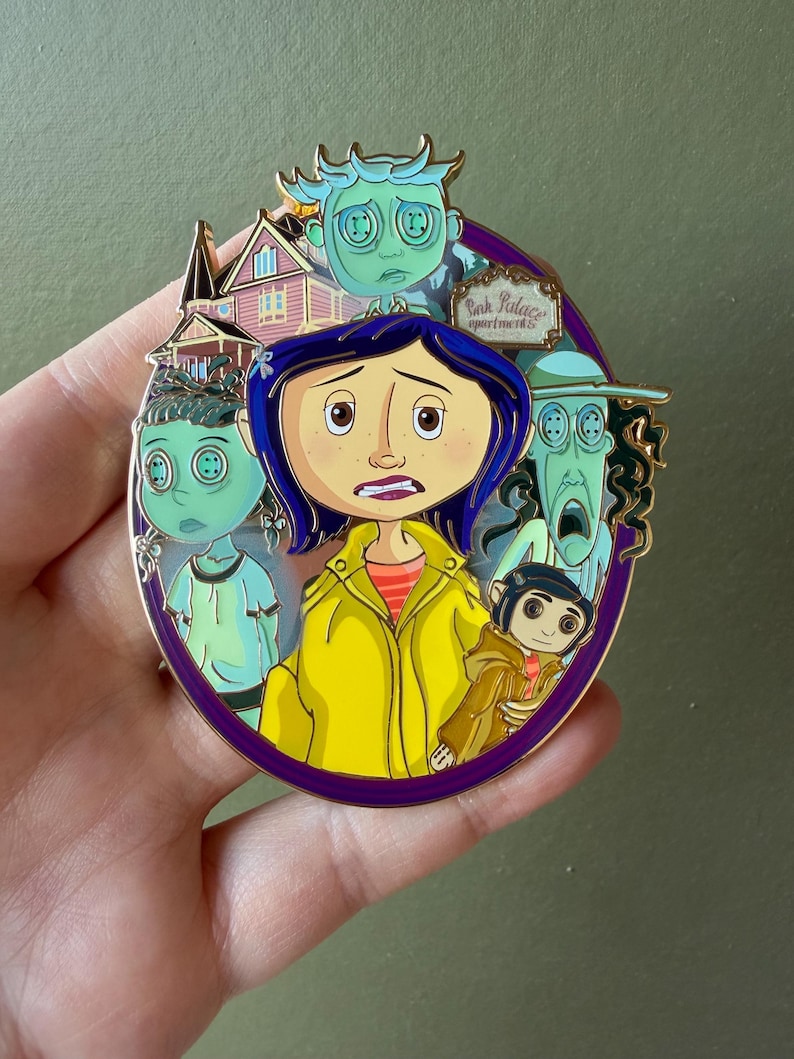 May include: A round enamel pin featuring characters from the animated film, "Coraline." The pin has a purple border and depicts the main character in a yellow raincoat, surrounded by other characters and the Pink Palace Apartments.