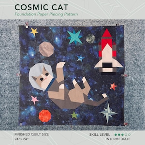 以下が含まれることがあります： 宇宙でロケットと星と一緒に浮いているヘルメットをかぶった猫を特徴とするキルトの基礎ペーパーピーシングパターン。完成したキルトのサイズは61cm×61cmです。スキルレベルは中級です。