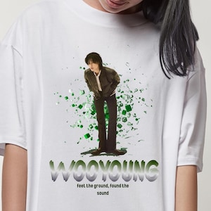 Puede incluir: Camiseta blanca con un gr&aacute;fico verde y blanco de una persona de pie con el texto "WOOYOUNG" y "Feel the ground, found the sound" debajo.