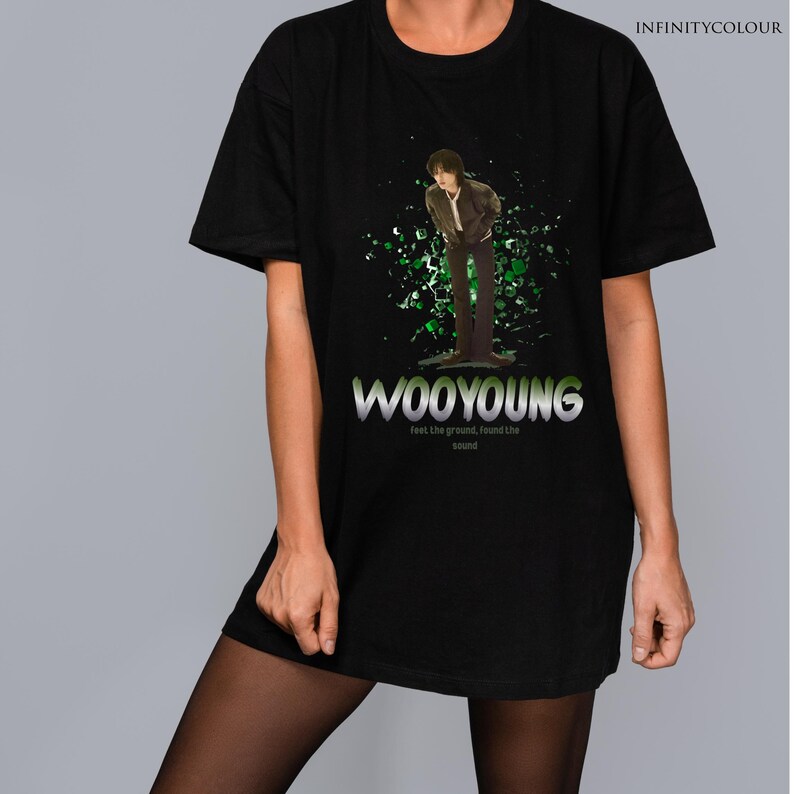Puede incluir: Camiseta negra con un estampado gr&aacute;fico de una persona de pie frente a un fondo verde. El texto "WOOYOUNG" est&aacute; impreso en letras plateadas debajo del gr&aacute;fico. El texto "Feet the ground, found the sound" est&aacute; impreso en letras plateadas m&aacute;s peque&ntilde;as debajo del nombre.