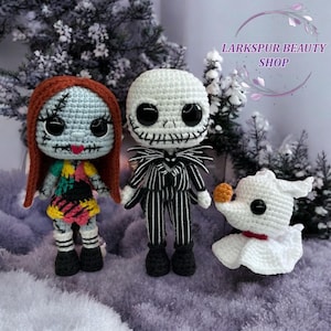 May include: Crocheted dolls of Sally, Jack Skellington, and Zero from The Nightmare Before Christmas. Sally has red hair, a patchwork dress, and stitched features. Jack is in a pinstripe suit. Zero is white with a pumpkin nose. The text "Larkspur Beauty Shop" is in the background.