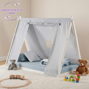 May include: A white wooden teepee-style bed frame with a light gray fabric canopy. The bed has a blue mattress, pillows, and a blanket. Two teddy bears, a wooden train set, and building blocks are placed around the bed. The text "Larkspur Beauty Shop" is in the top left corner.