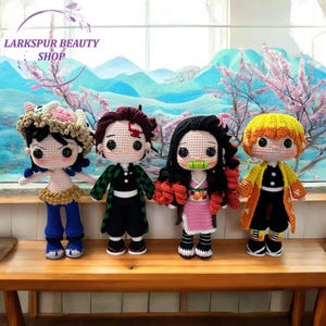 May include: Four handmade crochet dolls, each with unique outfits and hairstyles, stand on a wooden surface. The dolls are inspired by anime characters. The background features a scenic view with pink blossoms and a blue landscape. The shop name "Larkspur Beauty Shop" is visible.