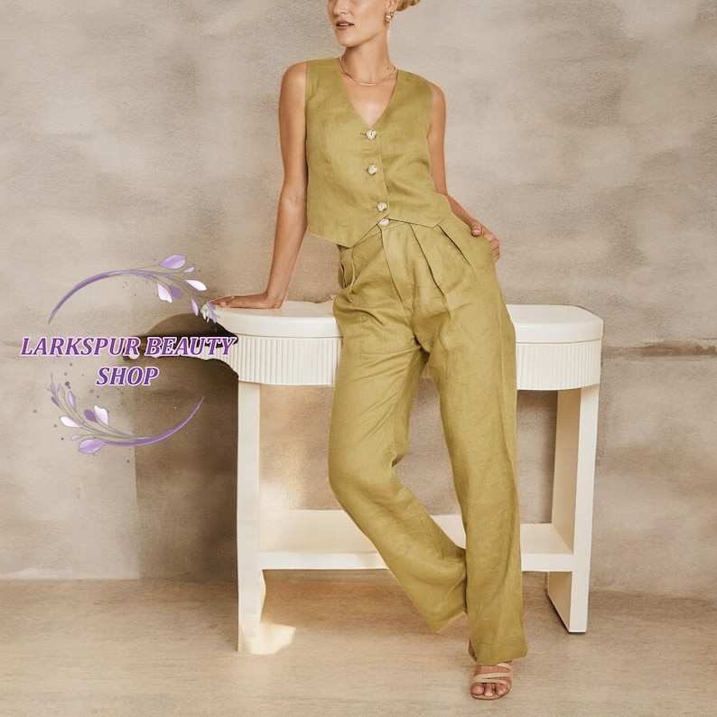 May include: An olive green linen suit comprising a sleeveless vest with button fastenings and wide-leg trousers. The outfit is worn with neutral sandals. The image includes the text "Larkspur Beauty Shop". The suit is suitable for warm weather.