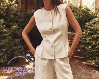 May include: A cream-colored sleeveless top with matching wide-leg pants. The top has a button-up front and a peplum-style waist. The outfit is made of a lightweight fabric. The text "Larkspur Beauty Shop" is visible in the image.