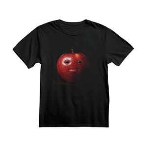 May include: Black t-shirt featuring a red apple with a face design. The apple has a stem and a smiling expression. The graphic is centered on the front of the shirt.