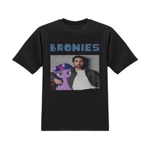 May include: Black t-shirt with the word "BRONIES" in blue block letters. The shirt features a graphic of a purple cartoon pony and a man in a blazer. The pony is next to the man, who is wearing a white shirt.