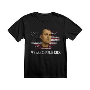 May include: Black t-shirt featuring a portrait of a man with an American flag design in the background. The text "WE ARE CHARLIE KIRK" is printed in white below the portrait. The shirt is made of a soft material.