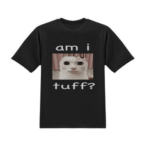 May include: Black t-shirt featuring a meme of a white cat with a pink bow. The text "am i tuff?" is printed above and below the cat image in white. The shirt is a short-sleeved crew neck.