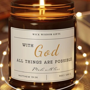 May include: A brown glass candle with a white label that reads "WICK WISDOM GIFTS", "WITH God", "ALL THINGS ARE POSSIBLE", "Made with love", "MATTHEW 19:26", and "9 OZ / 255 G". The candle is lit and sitting on a wooden coaster.