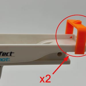 May include: A white plastic toy gun with the text "Perfect Shot" and an orange plastic component. The orange component is a rectangular shape with two vertical supports and a horizontal top. The image shows two of these orange components.