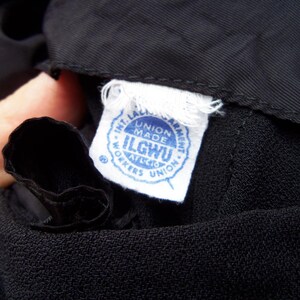 May include: Close-up of black fabric with a white tag. The tag has blue text that reads "INT. LADIES GARMENT WORKERS UNION MADE ILGWU AFL-CIO WORKERS UNION."