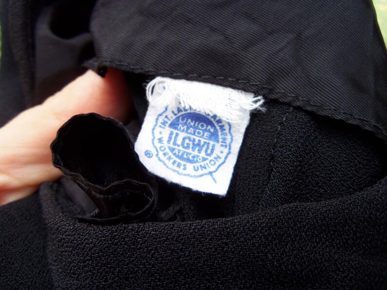 May include: Close-up of black fabric with a white tag. The tag has blue text that reads "INT. LADIES GARMENT WORKERS UNION MADE ILGWU AFL-CIO WORKERS UNION."