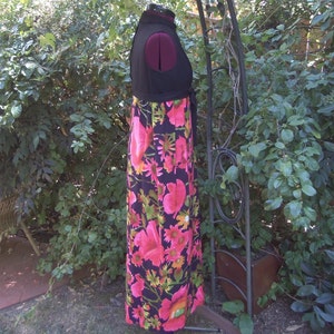 May include: A vintage maxi dress with a black bodice and a vibrant floral print skirt. The skirt features large pink flowers, green leaves, and yellow accents on a black background. The dress is displayed on a mannequin.