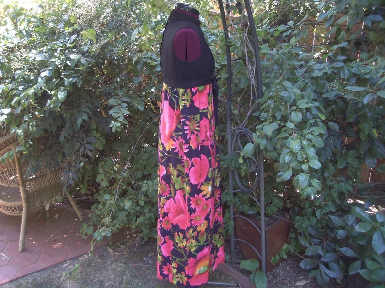 May include: A vintage maxi dress with a black bodice and a vibrant floral print skirt. The skirt features large pink flowers, green leaves, and yellow accents on a black background. The dress is displayed on a mannequin.