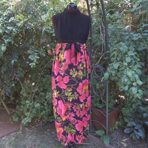 May include: A vintage maxi dress with a black bodice and a vibrant floral skirt. The skirt features large pink and yellow flowers on a dark background. A black tie belt cinches the waist. The dress is displayed on a mannequin.