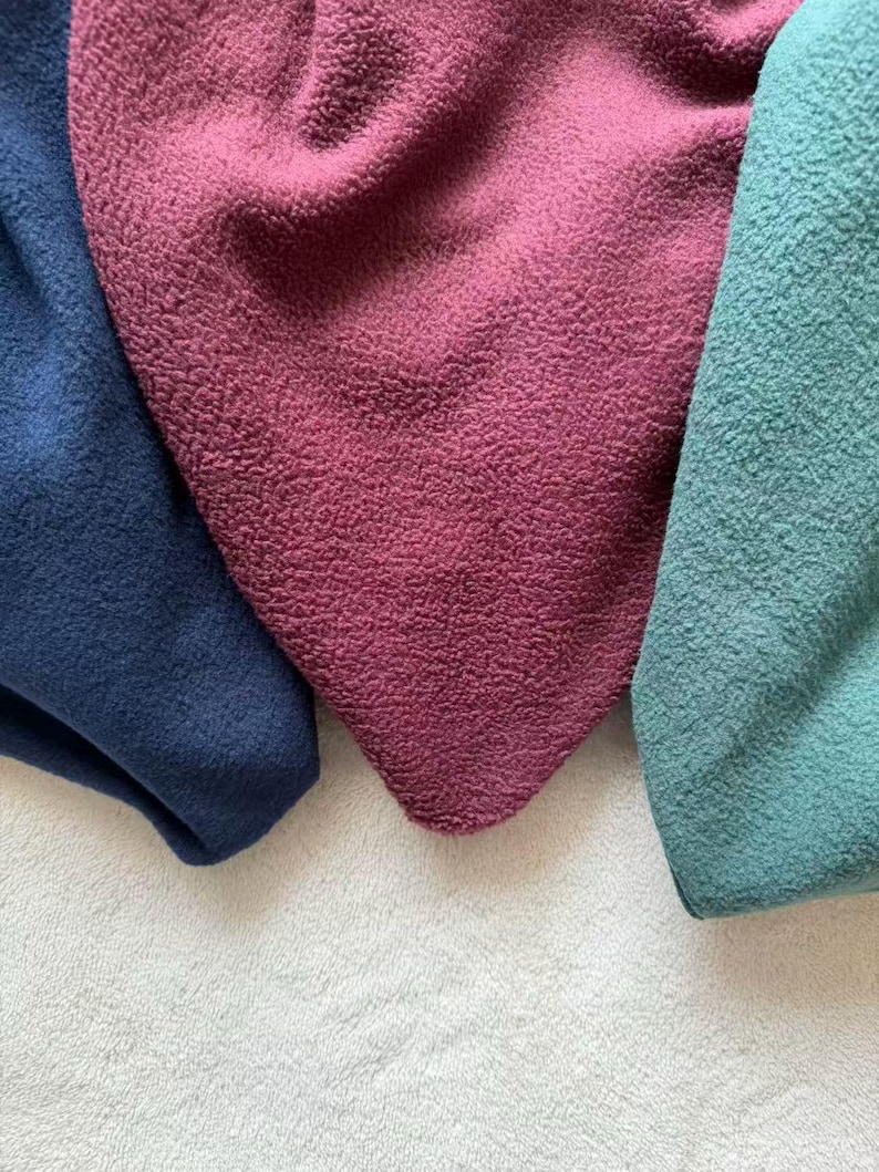 May include: Close-up of three pieces of textured fabric in shades of navy blue, burgundy, and teal. The fabrics are arranged on a white, textured surface, with the colors overlapping slightly. The texture appears soft and plush.